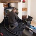 A man wearing protective mask checks a problematic fireplace in a home.