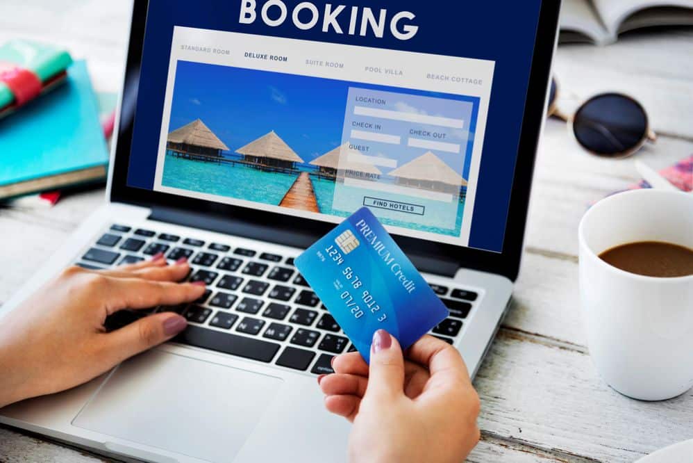 A person booking a beach resort online using a laptop and credit card — planning an affordable 4-star resort stay.